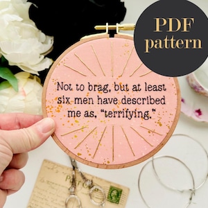 May include: A pink embroidery hoop with gold detailing and the quote "Not to brag, but at least six men have described me as, 'terrifying.'" A black circle with "PDF pattern" is in the upper right. Other items are in the background.