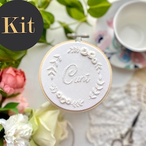 Op de afbeelding: Een witte borduurring met een bloemenontwerp en het woord "Curt" geborduurd in witte draad.