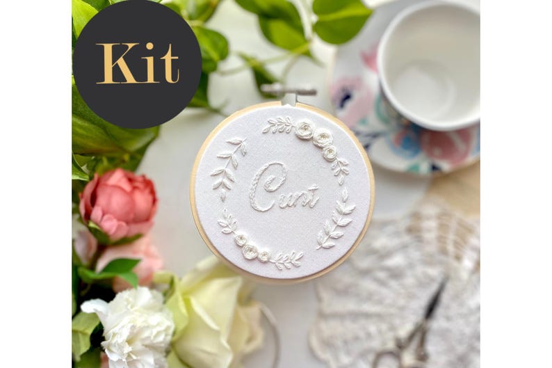 Op de afbeelding: Een witte borduurring met een bloemenontwerp en het woord "Curt" geborduurd in witte draad.