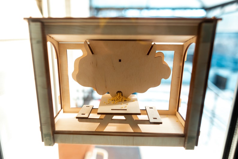 Peut inclure: Une mangeoire &agrave; oiseaux en bois avec un toit en forme de nuage et une petite table de pique-nique en dessous. La mangeoire est remplie de graines d'oiseaux jaunes.