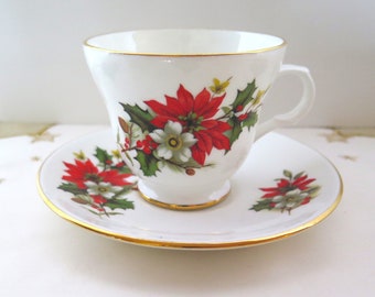 Könnte beinhalten: Weißes Tee-Set mit Tasse und Untertasse, goldfarben umrandet. Die Tasse und Untertasse sind mit einem Poinsettia- und Stechpalmen-Design in Rot, Weiß und Grün verziert. Ein klassisches Tee-Set zum Thema Weihnachten.