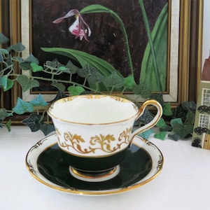 May include: A white teacup and saucer with gold trim and a green band. The saucer has a green centre and a gold rim. The teacup has a gold floral design.