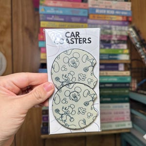 May include: Two round car coasters with a white background and a black outline of Mickey Mouse. The coasters have the text "CAR COASTERS" printed on the packaging.
