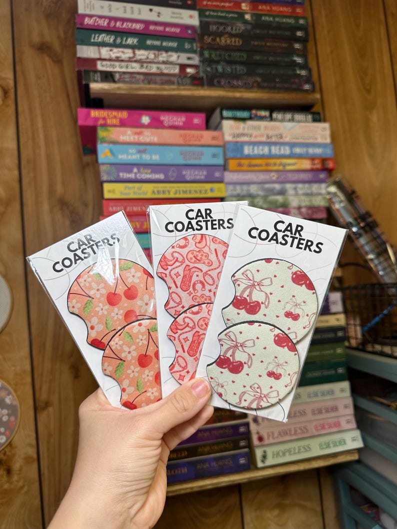 May include: Three sets of car coasters with a cherry and floral design. Each set includes two coasters. The coasters are made of a cork-like material and have a white background with red cherries and pink flowers.