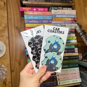 May include: Two sets of car coasters. One set features a black and white skull and crossbones design. The other set features a green and blue design with a cartoon character from the movie My Neighbor Totoro.