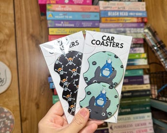 May include: Two sets of car coasters. One set features a black and white skull and crossbones design. The other set features a green and blue design with a cartoon character from the movie My Neighbor Totoro.