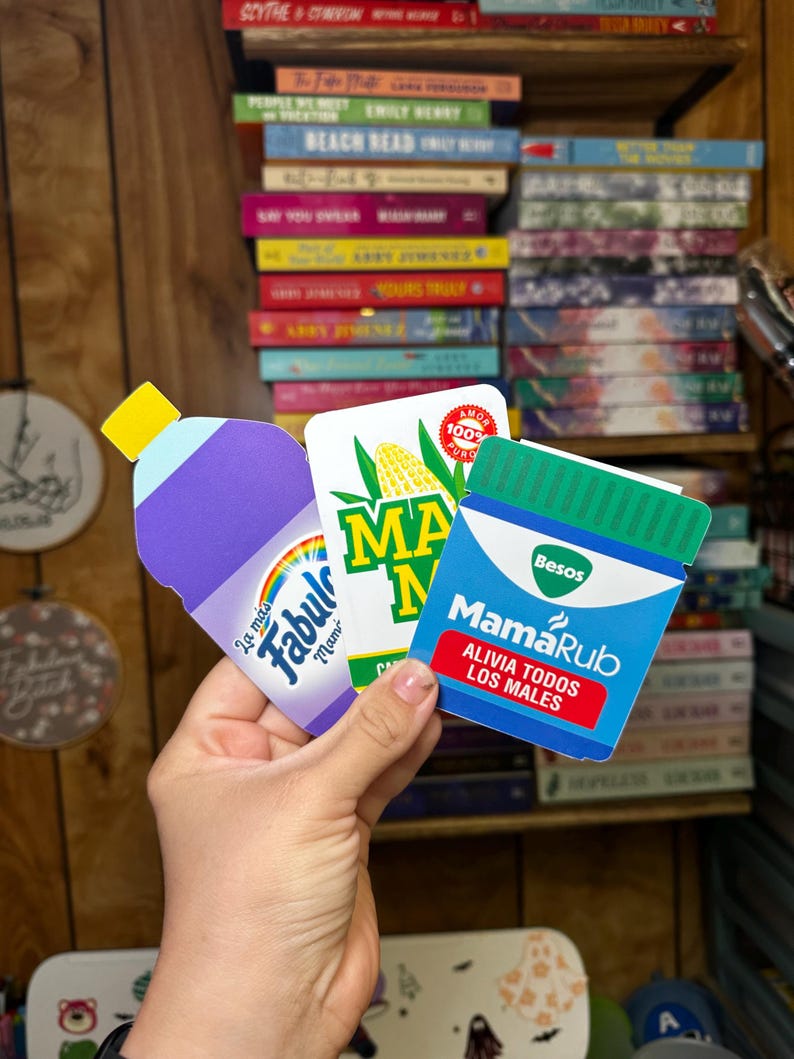 May include: Three colorful product packaging mockups. A purple bottle with a rainbow and the text "La m&aacute;s Fabul Mam" on it. A yellow and green package with the text "MA" and "100% PURO" on it. A blue and green package with the text "Besos MamaRub ALIVIA TODOS LOS MALES" on it.