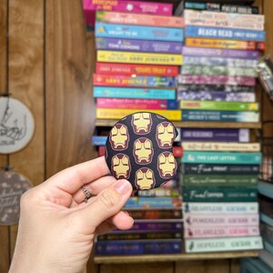 May include: A round, black and yellow car coaster with a repeating pattern of Iron Man's mask.