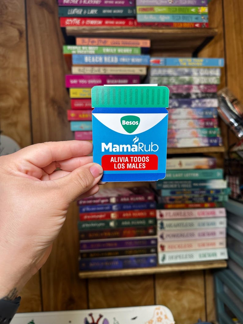 May include: A blue and white sticker with the text "MamaRub" and "Alivia Todos Los Males" in a blue box. The sticker is shaped like a bottle with a green lid and the text "Besos" in a white box.