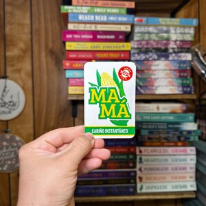 May include: A white sticker with green and yellow corn on it. The sticker says "MA MA" and "CARI&Ntilde;O INSTANT&Aacute;NEO". There is a red circle with the words "AMOR 100% PURO" on it.