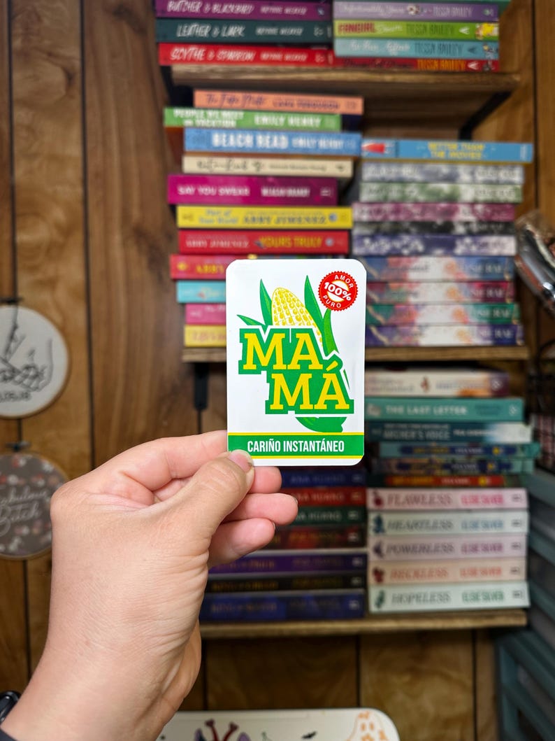 May include: A white sticker with green and yellow corn on it. The sticker says "MA MA" and "CARI&Ntilde;O INSTANT&Aacute;NEO". There is a red circle with the words "AMOR 100% PURO" on it.