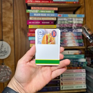 May include: A white card with green and yellow stripes on the bottom edge. The card has the words "CARD" and "Subway" printed on it. A photo of a sandwich is visible on the card.