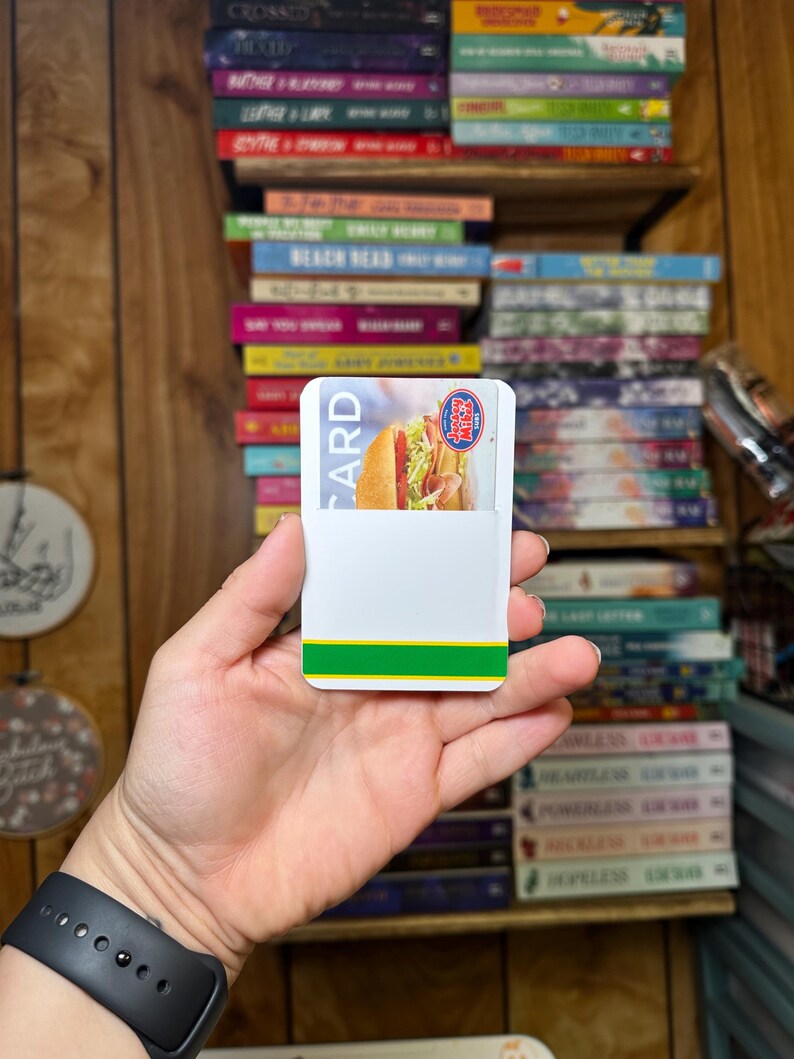 May include: A white card with green and yellow stripes on the bottom edge. The card has the words "CARD" and "Subway" printed on it. A photo of a sandwich is visible on the card.