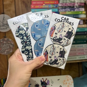 May include: Three sets of car coasters featuring different designs. The first set features a black and white pattern with a spooky theme. The second set features a blue and white pattern with a cartoon character. The third set features a white and black pattern with a cartoon character from a Disney movie. The text on the packaging reads "Car Coasters".