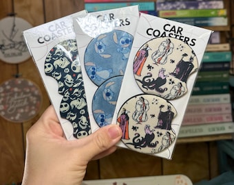 May include: Three sets of car coasters featuring different designs. The first set features a black and white pattern with a spooky theme. The second set features a blue and white pattern with a cartoon character. The third set features a white and black pattern with a cartoon character from a Disney movie. The text on the packaging reads "Car Coasters".