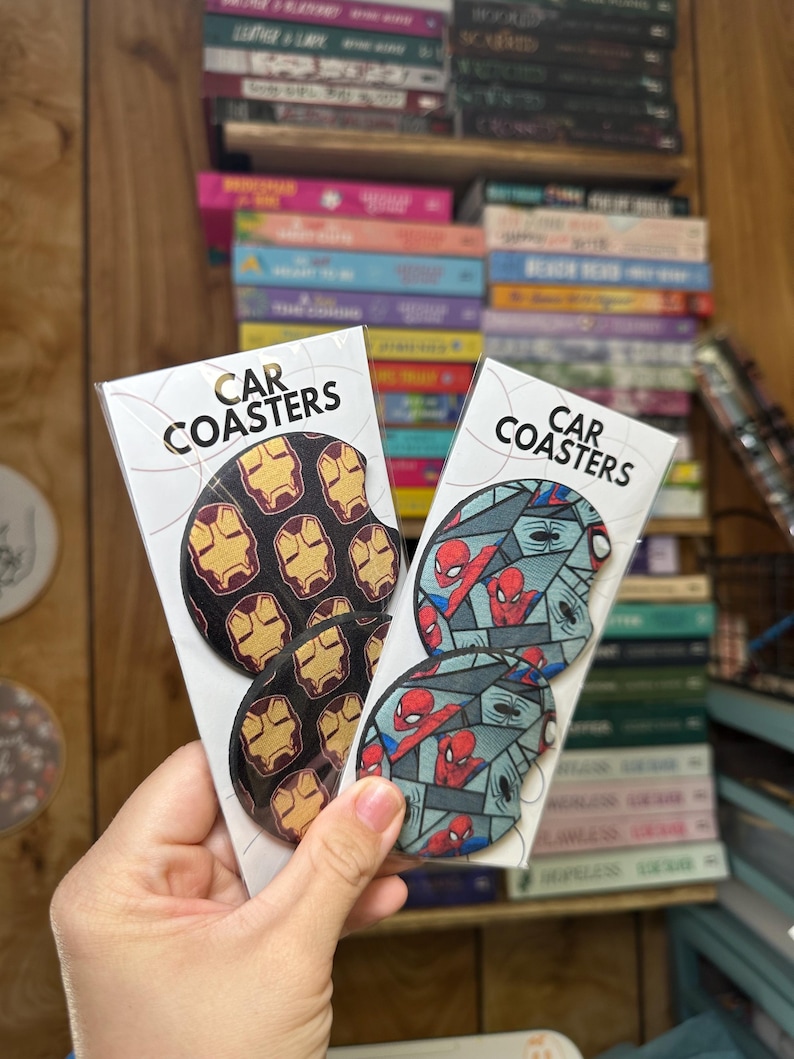May include: Two sets of car coasters featuring popular superhero characters. One set features Iron Man's mask in a repeating pattern on a black background. The other set features Spider-Man in a repeating pattern on a blue and gray background. The coasters are packaged in clear plastic.