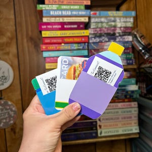 May include: A hand holds three gift cards. The cards are blue, purple, and white. The blue card has a QR code and the text "To Connect!" The purple card has a QR code and the text "To Connect!" The white card has a picture of a hamburger and the text "CARD".
