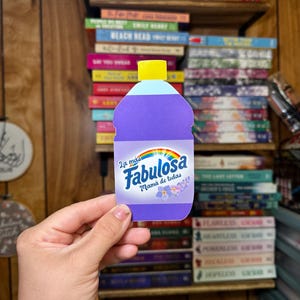 May include: A purple bottle with a yellow lid and a rainbow design. The bottle has the text "La mas Fabulosa Mama de todas" on it.