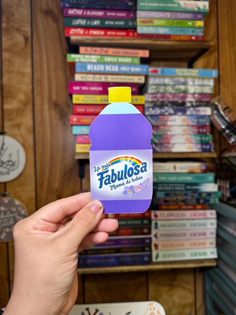 May include: A purple bottle with a yellow lid and a rainbow design. The bottle has the text "La mas Fabulosa Mama de todas" on it.