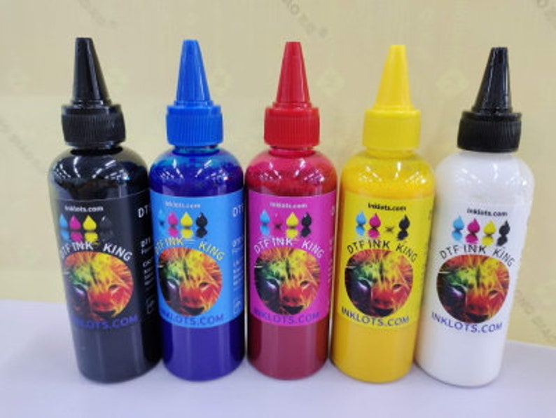 Pode incluir: Quatro garrafas de tinta DTF, cada uma com uma cor diferente: preto, azul, vermelho e amarelo. As garrafas s&atilde;o etiquetadas com "DT Ink King" e t&ecirc;m um endere&ccedil;o de site no r&oacute;tulo.