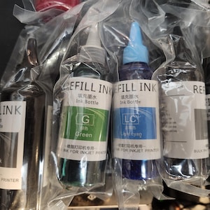 May include: Four bottles of ink refill for inkjet printers. The bottles are labeled with the colors green, light cyan, and light black. The bottles are in clear plastic packaging.