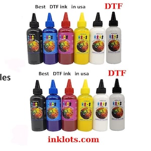 May include: Twelve bottles of DTF ink, labeled "Dye Ink King", in black, blue, red, yellow, white, and gray. The bottles are arranged in two rows of six. The text "Best DTF ink in usa" and "DTF" are printed above the bottles. The text "inklots.com" is printed below the bottles.