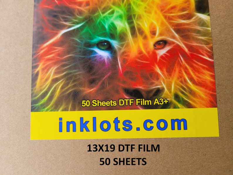 Pode incluir: Um pacote de 50 folhas de filme DTF A3+ para uso com uma impressora direta para filme. O pacote tem uma imagem colorida de um rosto de le&atilde;o na frente e o texto "inklots.com" em letras azuis sobre um fundo amarelo. O texto "50 Sheets DTF Film A3+" tamb&eacute;m &eacute; vis&iacute;vel na frente do pacote.