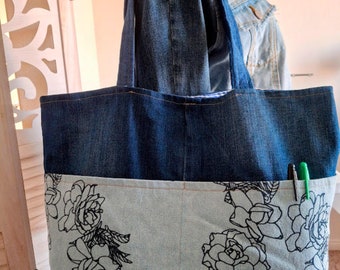 May include: A blue denim tote bag with a light blue floral print on the bottom half. The bag has two long denim straps.