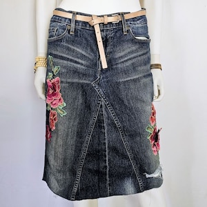 May include: A dark blue denim skirt with a brown belt and floral embroidery. The skirt has a distressed look with a ripped hem.