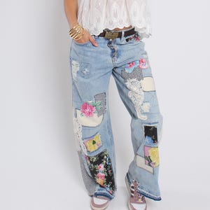 Könnte beinhalten: Hellblaue Jeans mit mehreren Stoffflicken mit Blumen- und Mustermotiven. Zu den Flicken gehören rosa Rosen, gelbe Blumen und schwarz-weiß karierte Muster. Die Jeans hat eine lockere Passform und wird mit einem braunen Gürtel und einer goldenen Schnalle getragen.