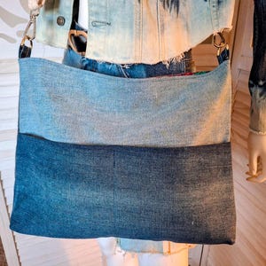May include: A blue denim tote bag with a light blue denim top section and a dark blue denim bottom section. The bag has a long strap and is made from recycled denim.