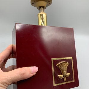 May include: A burgundy lamp base with a gold trim and a gold lotus flower design. The lamp base has a gold metal top for attaching a lampshade.