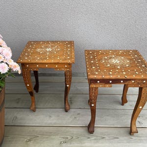 May include: Two square wooden side tables featuring intricate light-colored inlay patterns on the top surfaces and legs. The tables have curved legs and a warm brown wood grain finish, with small diamond-shaped accents embedded into the wood.