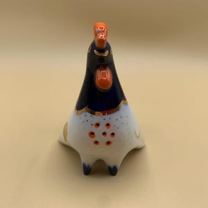 May include: A blue and white ceramic rooster figurine with orange accents. The rooster has a gold trim around its neck and a white body with orange dots.
