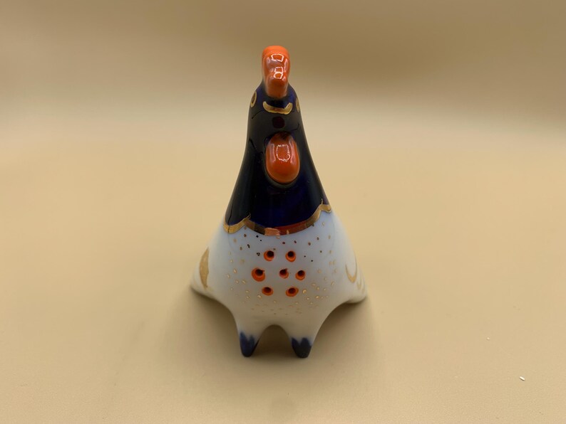 May include: A blue and white ceramic rooster figurine with orange accents. The rooster has a gold trim around its neck and a white body with orange dots.