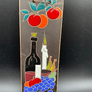 May include: A ceramic tile featuring a still life design with a bottle of wine, grapes, a candle, and fruit. The tile is brown with colourful accents.