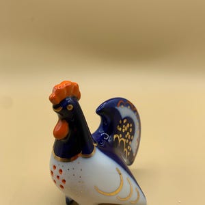 May include: A blue and white porcelain rooster figurine with gold accents. The rooster has an orange comb and wattle.