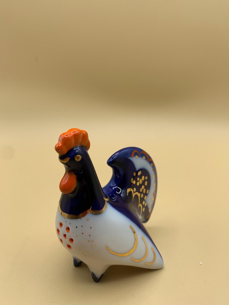 May include: A blue and white porcelain rooster figurine with gold accents. The rooster has an orange comb and wattle.