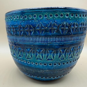 May include: A deep blue ceramic bowl featuring a textured surface with horizontal bands of embossed geometric patterns, including repeating diamond shapes, vertical lines, and small circular indentations, finished with a glossy glaze.
