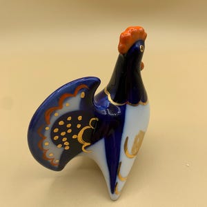 May include: A blue and white porcelain rooster figurine with gold accents. The rooster has an orange comb and wattle.