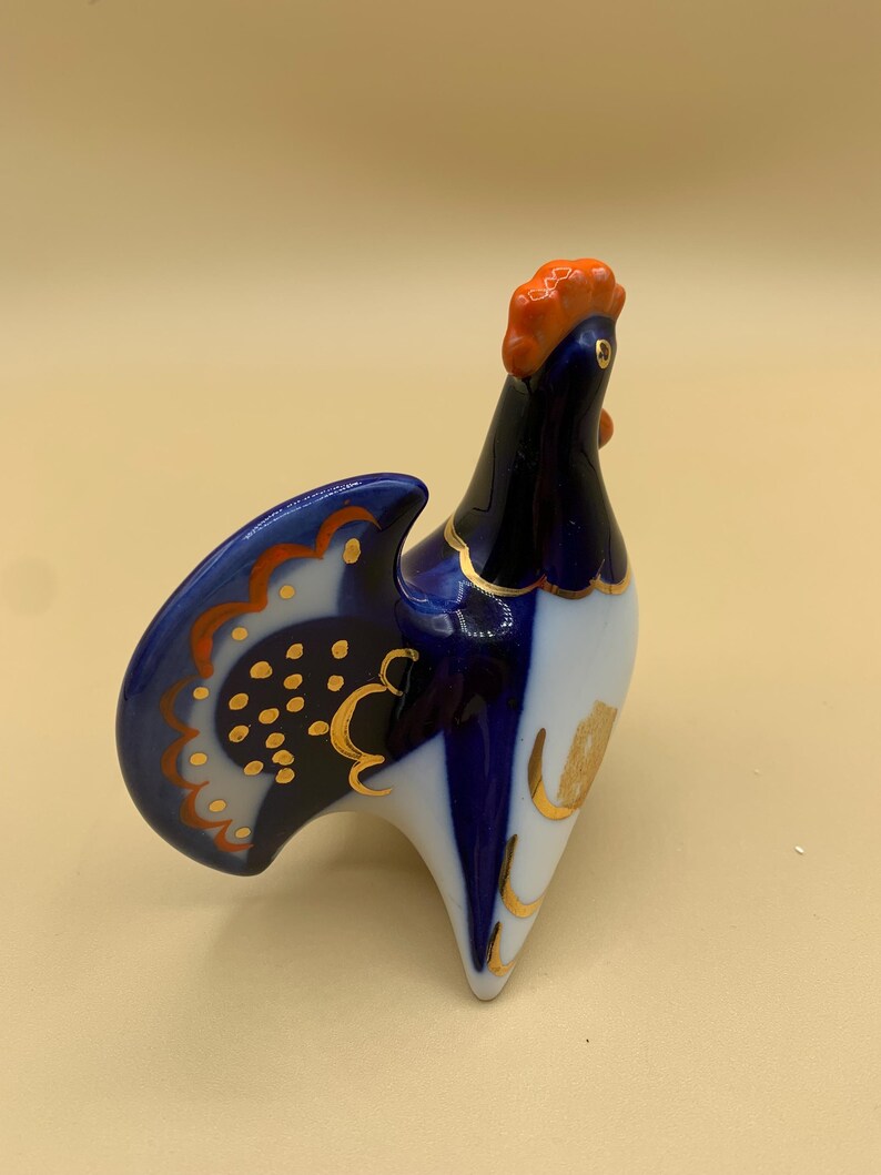 May include: A blue and white porcelain rooster figurine with gold accents. The rooster has an orange comb and wattle.