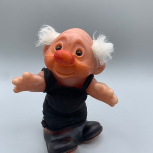 May include: A vintage troll doll with white hair, a black jumpsuit, and brown shoes. The troll has a large red nose and a friendly expression.