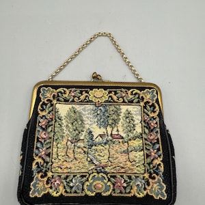 Pode incluir: Bolsa de mão vintage em tapeçaria preta com alça de corrente dourada. A tapeçaria apresenta uma cena detalhada de paisagem com árvores, uma casa e figuras, emoldurada por bordas florais e de rolagem. A bolsa tem um fecho dourado.