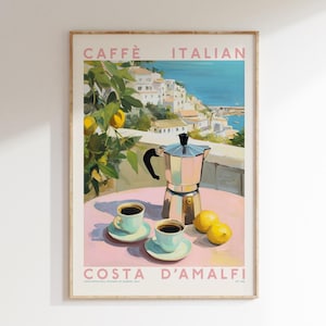 May include: A framed print with the text "CAFFÈ ITALIAN" and "COSTA D'AMALFI". The image depicts a silver coffee maker, two cups of coffee, and lemons on a pink table. The background shows a coastal Italian town, evoking a sense of place and leisure.