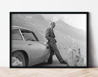 Könnte beinhalten: Ein Schwarzweißfoto eines Mannes im Anzug, der neben einem klassischen Auto in einer Berglandschaft steht.