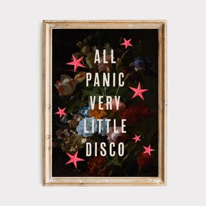 May include: A framed art print with a floral still life against a dark backdrop. The print displays the text "ALL PANIC VERY LITTLE DISCO" in white, with pink star accents. The frame is a light brown colour.
