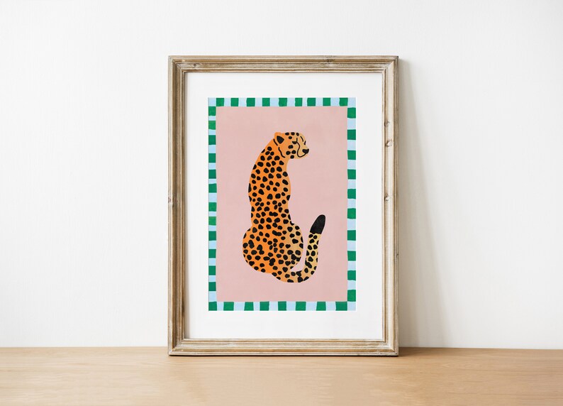 May include: A framed print of a cheetah sitting on a pink background with a green and blue checkered border.