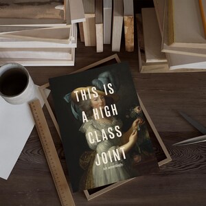 K&ouml;nnte beinhalten: Kunstdruck mit einem Portr&auml;t einer Frau in historischer Kleidung und dem Text "THIS IS A HIGH CLASS JOINT". Der Druck befindet sich in einem Holzrahmen, mit einem Lineal und einer Tasse in der N&auml;he.