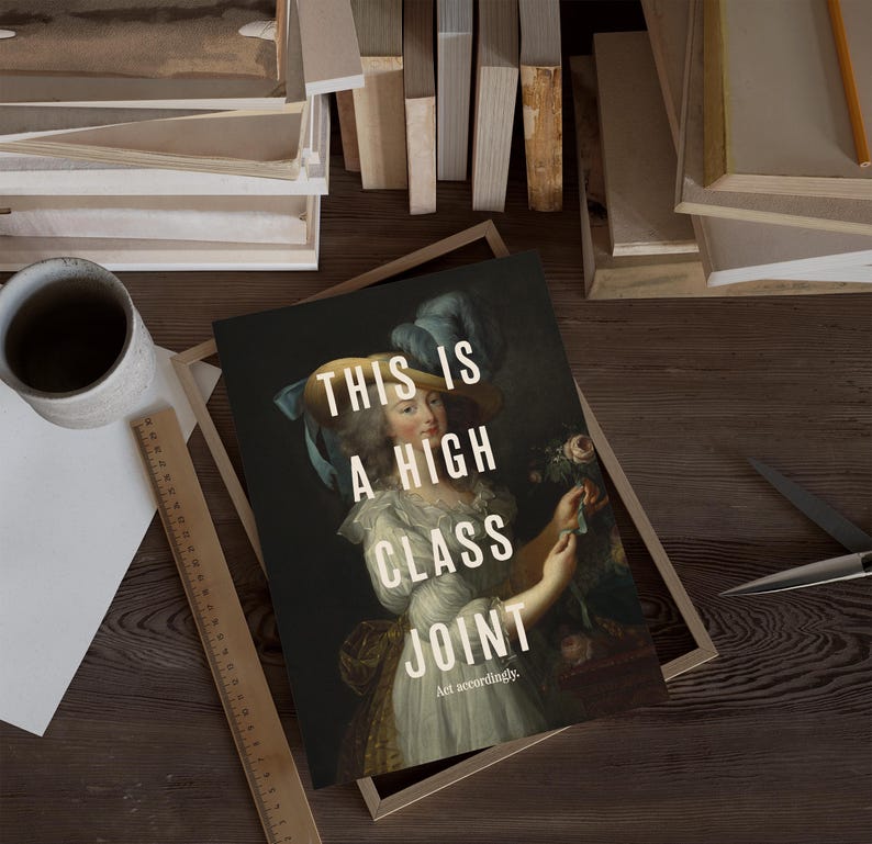 K&ouml;nnte beinhalten: Kunstdruck mit einem Portr&auml;t einer Frau in historischer Kleidung und dem Text "THIS IS A HIGH CLASS JOINT". Der Druck befindet sich in einem Holzrahmen, mit einem Lineal und einer Tasse in der N&auml;he.
