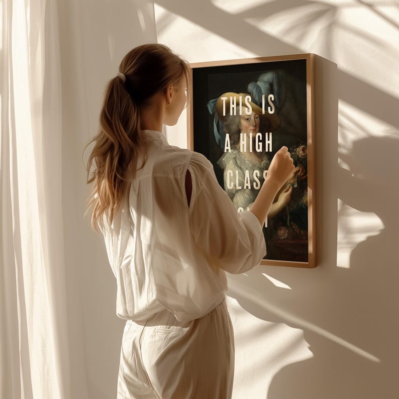 K&ouml;nnte beinhalten: Ein gerahmter Kunstdruck mit einem klassischen Portr&auml;t und dem Text "THIS IS A HIGH CLASS" in Wei&szlig;. Das Kunstwerk befindet sich in einem Holzrahmen. Eine Person in einem wei&szlig;en Hemd und einer Hose h&auml;lt den gerahmten Druck.